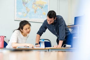 A teacher points to a text book to help explain to a student. Adult class at Studio Cambridge